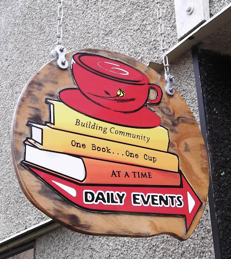 Sign with Coffee cup on top of books reading "Building Community One Book,, One Cup, at a time. Daily Events"